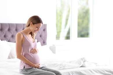 Happy pregnant woman sitting in bed at home