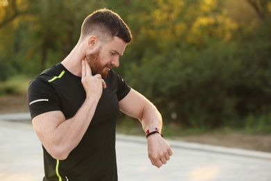 Photo of Young man checking pulse after workout in park