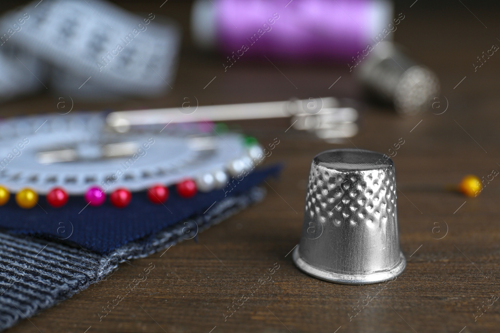 Photo of Silver thimble near sewing tools on wooden table, closeup. Space for text