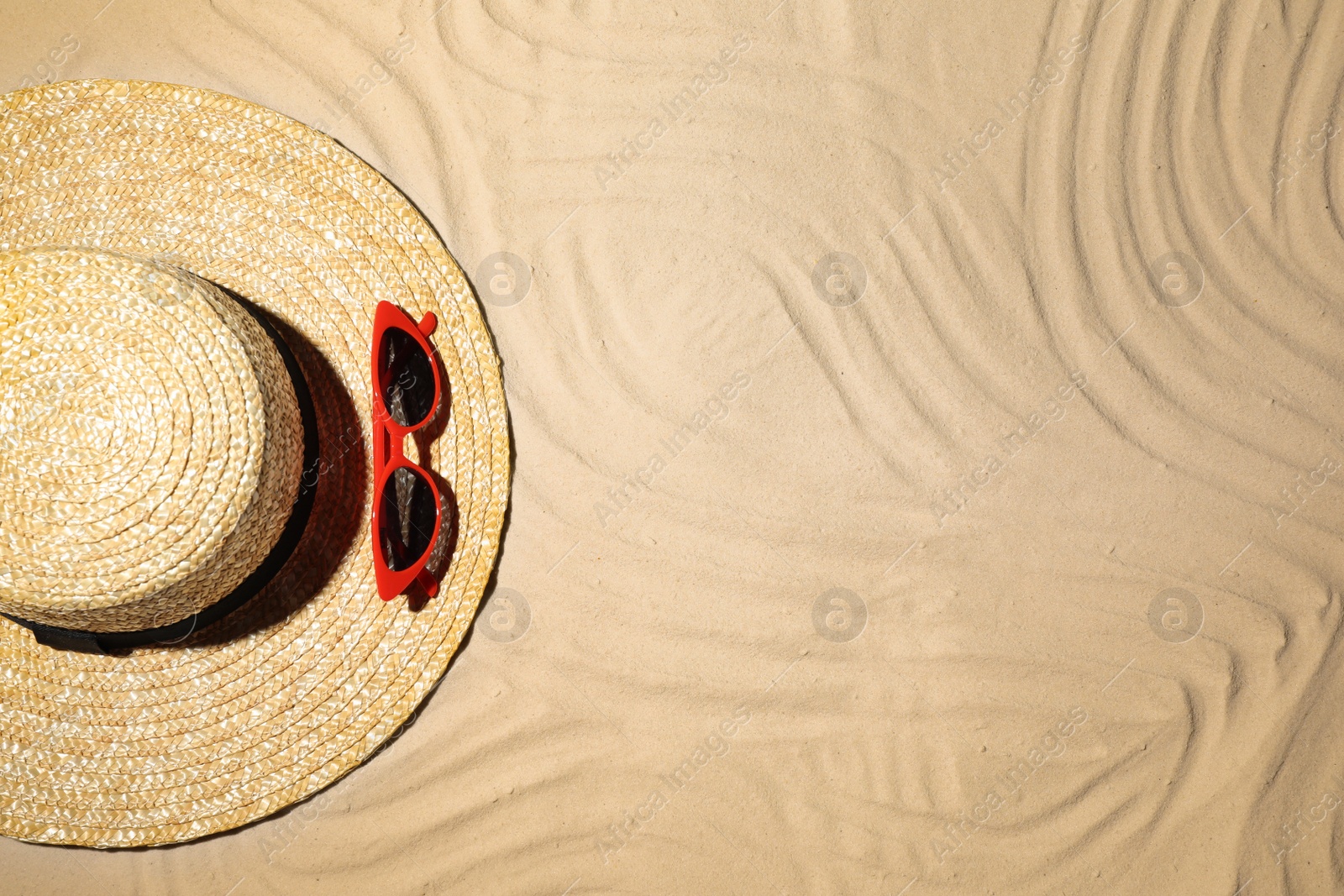 Photo of Straw hat and sunglasses on sand, top view. Beach accessories