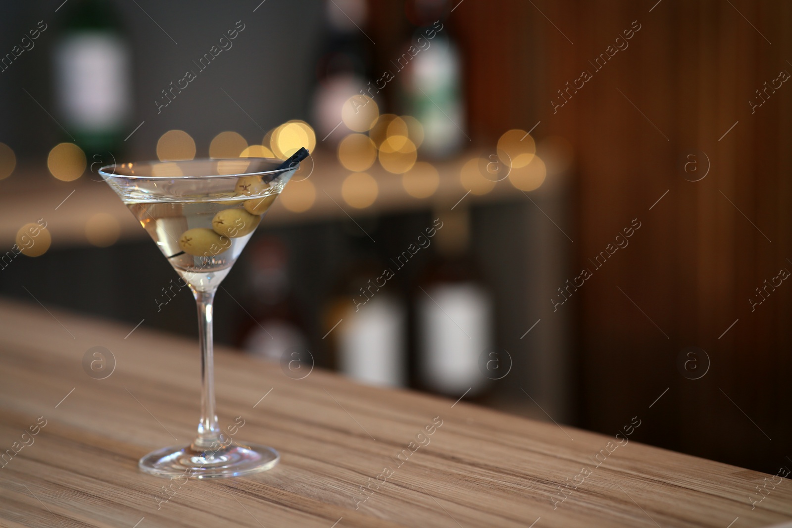 Photo of Delicious martini cocktail with olives on table in bar, space for text