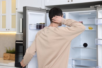 Man near empty refrigerator in kitchen at home, back view