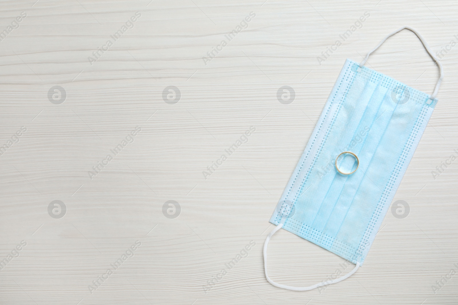 Photo of Protective mask and wedding ring on white wooden table, flat lay with space for text. Divorce during coronavirus quarantine