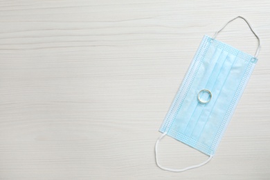 Protective mask and wedding ring on white wooden table, flat lay with space for text. Divorce during coronavirus quarantine