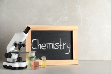 Laboratory glassware, microscope and board with word CHEMISTRY on table against grey background. Space for text