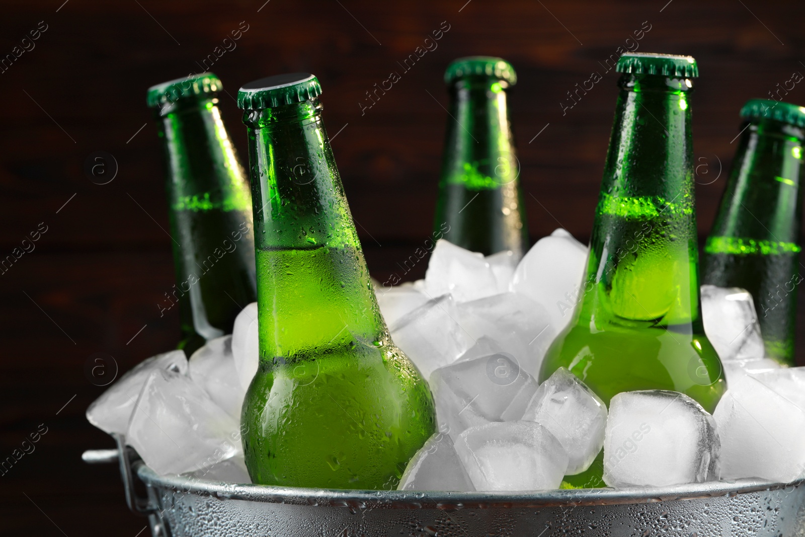 Photo of Metal bucket with bottles of beer and ice cubes on wooden background, closeup