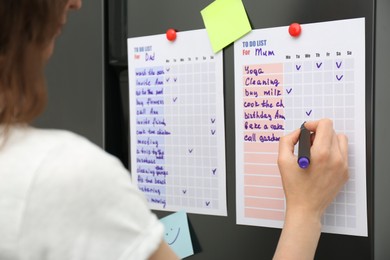 Photo of Woman checking to do list on refrigerator door in kitchen, closeup