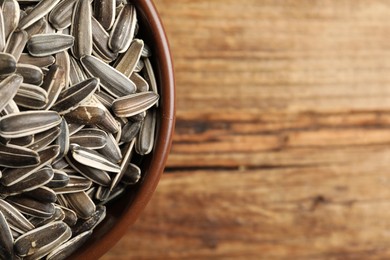 Photo of Raw sunflower seeds in bowl on wooden table, closeup. Space for text