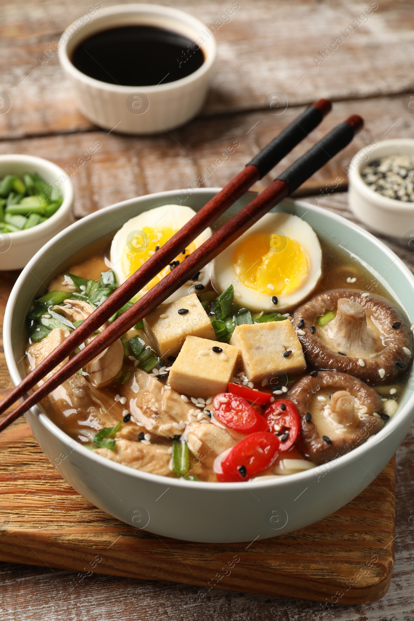 Photo of Noodle soup. Bowl of delicious ramen and chopsticks on wooden table, closeup