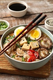 Photo of Noodle soup. Bowl of delicious ramen and chopsticks on wooden table, closeup