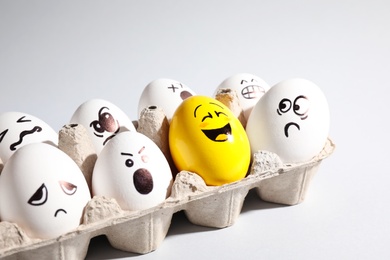 Photo of Yellow smiley egg among others with negative emotions in package on light background