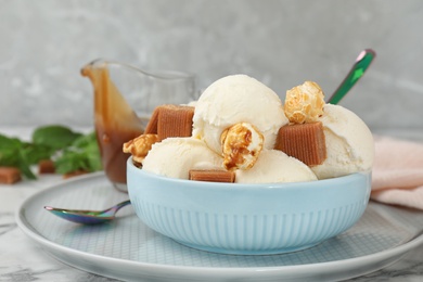Photo of Plate of delicious ice cream with caramel candies and popcorn on table