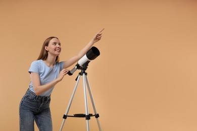Young astronomer with telescope pointing at something on beige background, low angle view. Space for text