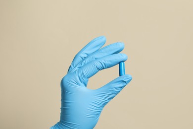 Photo of Doctor holding pill on beige background, closeup