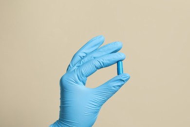 Doctor holding pill on beige background, closeup