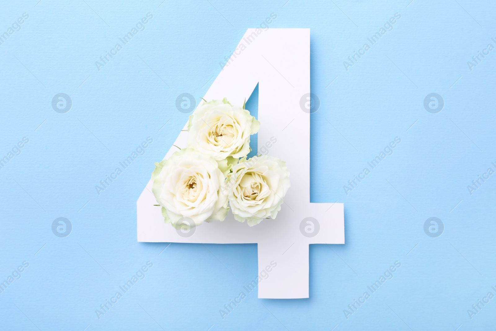 Photo of Paper number 4 and beautiful flowers on light blue background, top view