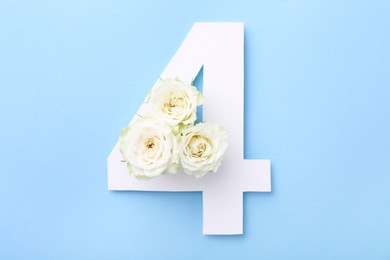 Photo of Paper number 4 and beautiful flowers on light blue background, top view