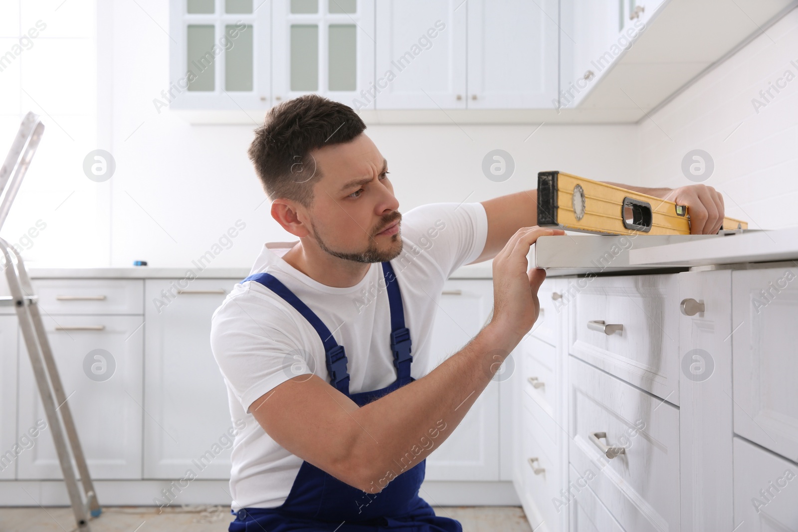 Photo of Worker measuring countertop with spirit level in kitchen