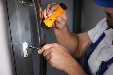 Photo of Repairman with flashlight fixing door lock, closeup