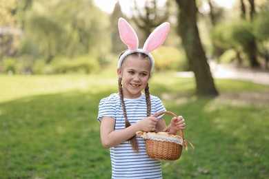 Photo of Easter celebration. Cute little girl in bunny ears holding wicker basket outdoors