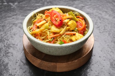 Photo of Stir-fry. Tasty noodles with vegetables and meat in bowl on dark textured table