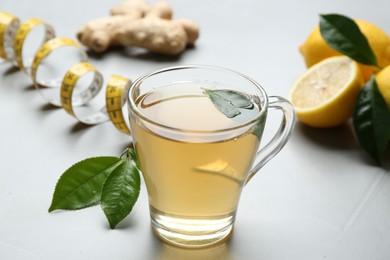 Photo of Herbal diet tea, lemon, ginger and measuring tape on light table