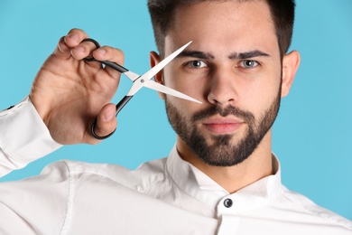 Young hairstylist holding professional scissors on color background, closeup