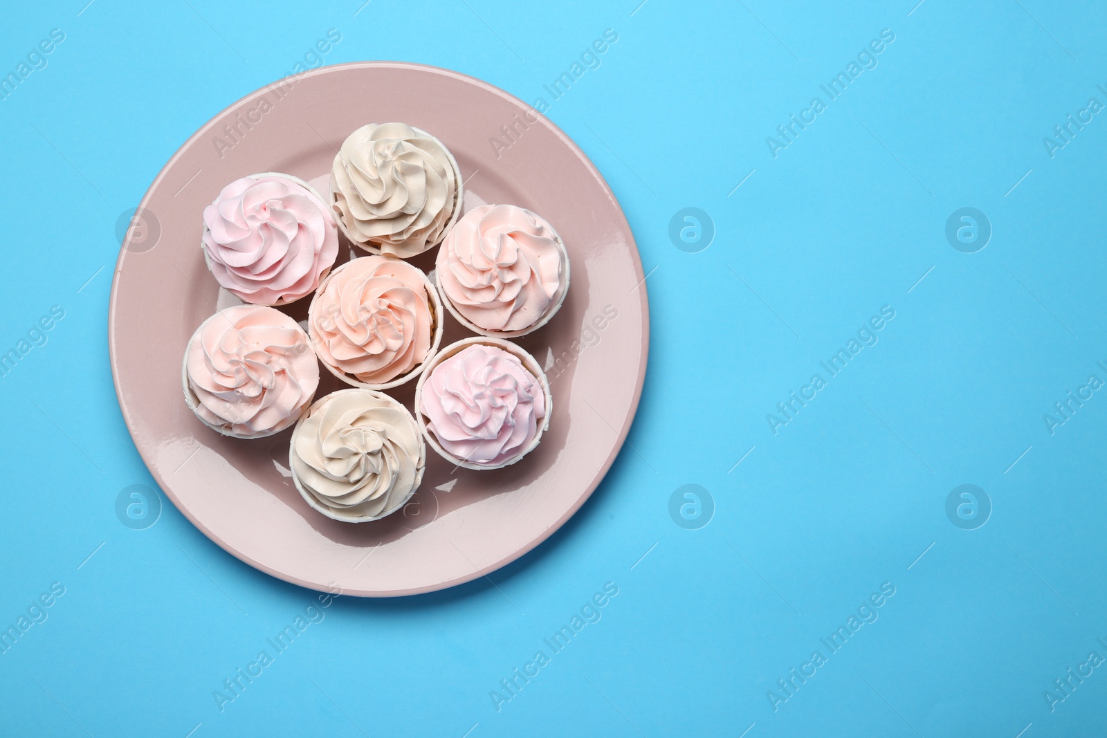 Photo of Plate with tasty cupcakes on light blue background, top view. Space for text
