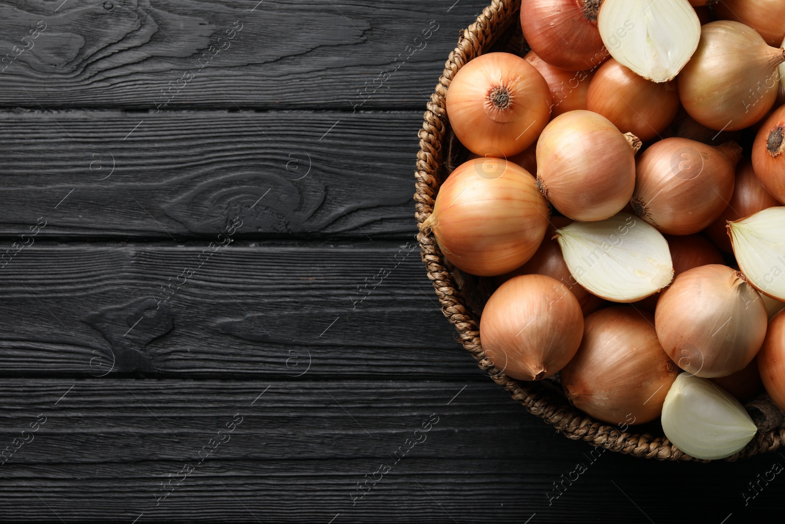 Photo of Whole and cut onions on black wooden table, top view. Space for text