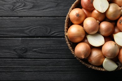 Whole and cut onions on black wooden table, top view. Space for text