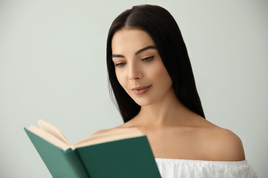 Photo of Beautiful young woman reading book on light grey background