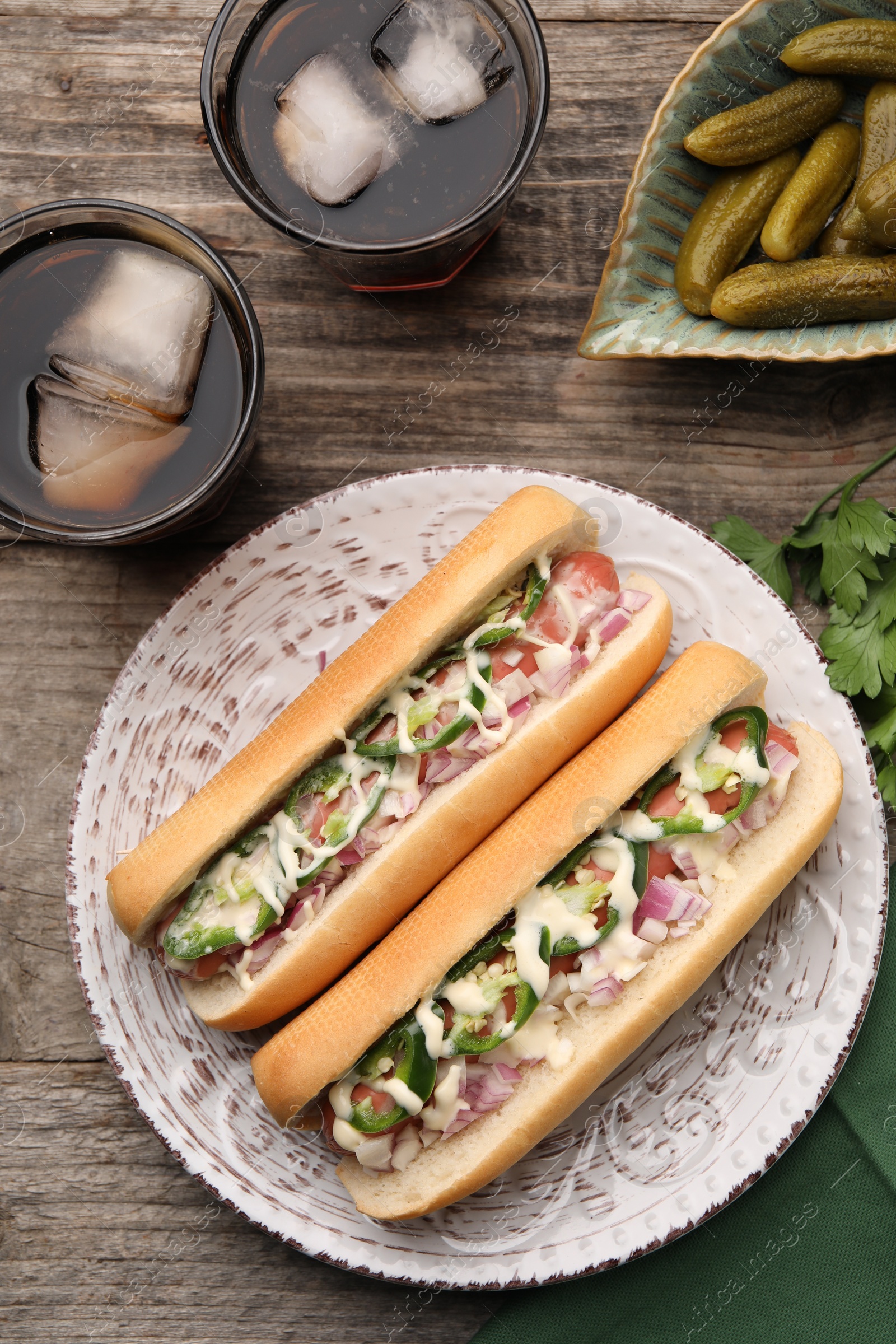 Photo of Delicious hot dogs with onion, chili pepper and sauce served on wooden table, flat lay