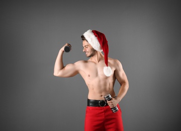 Photo of Shirtless sexy young Santa Claus with dumbbells on color background