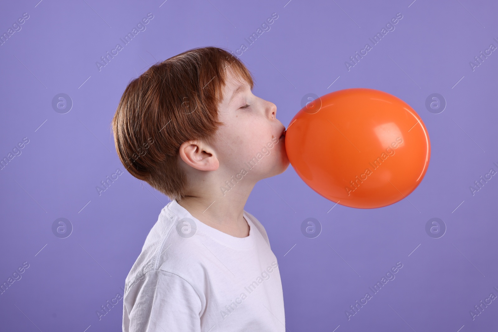 Photo of Boy inflating orange balloon on violet background