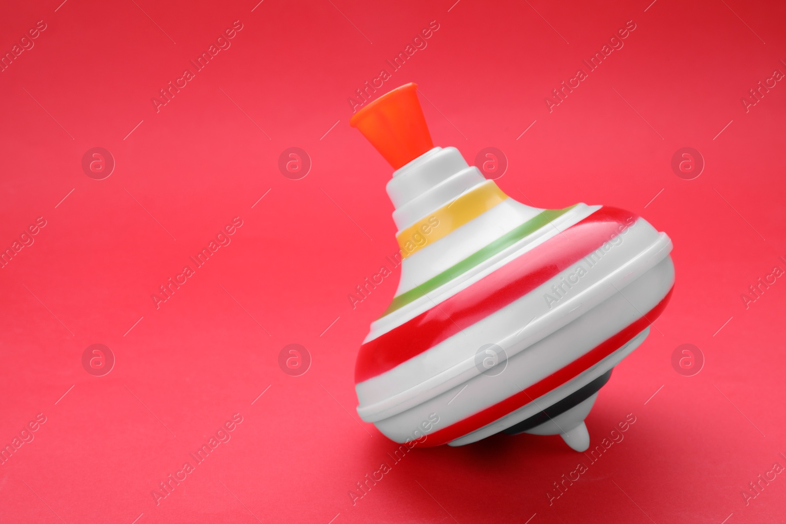 Photo of One bright spinning top on red background, space for text. Toy whirligig