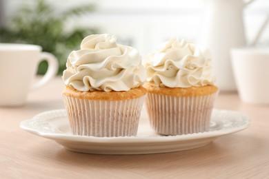 Tasty cupcakes with vanilla cream on light wooden table, closeup