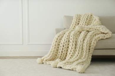 Knitted merino wool plaid on sofa near light wall. Space for text