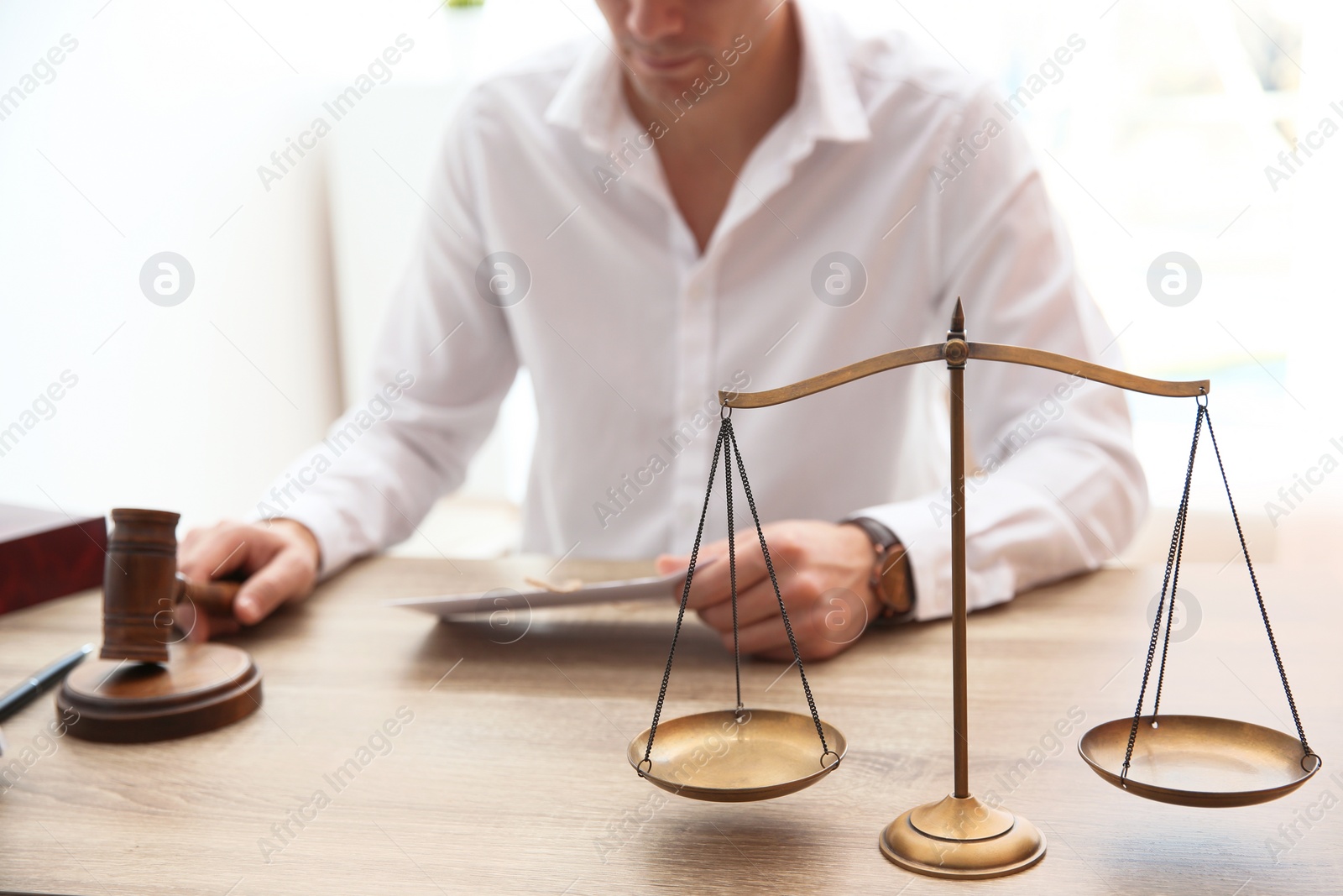 Photo of Judge working at table in courtroom, focus on scales of justice. Law concept