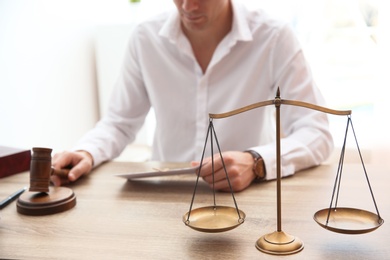 Photo of Judge working at table in courtroom, focus on scales of justice. Law concept