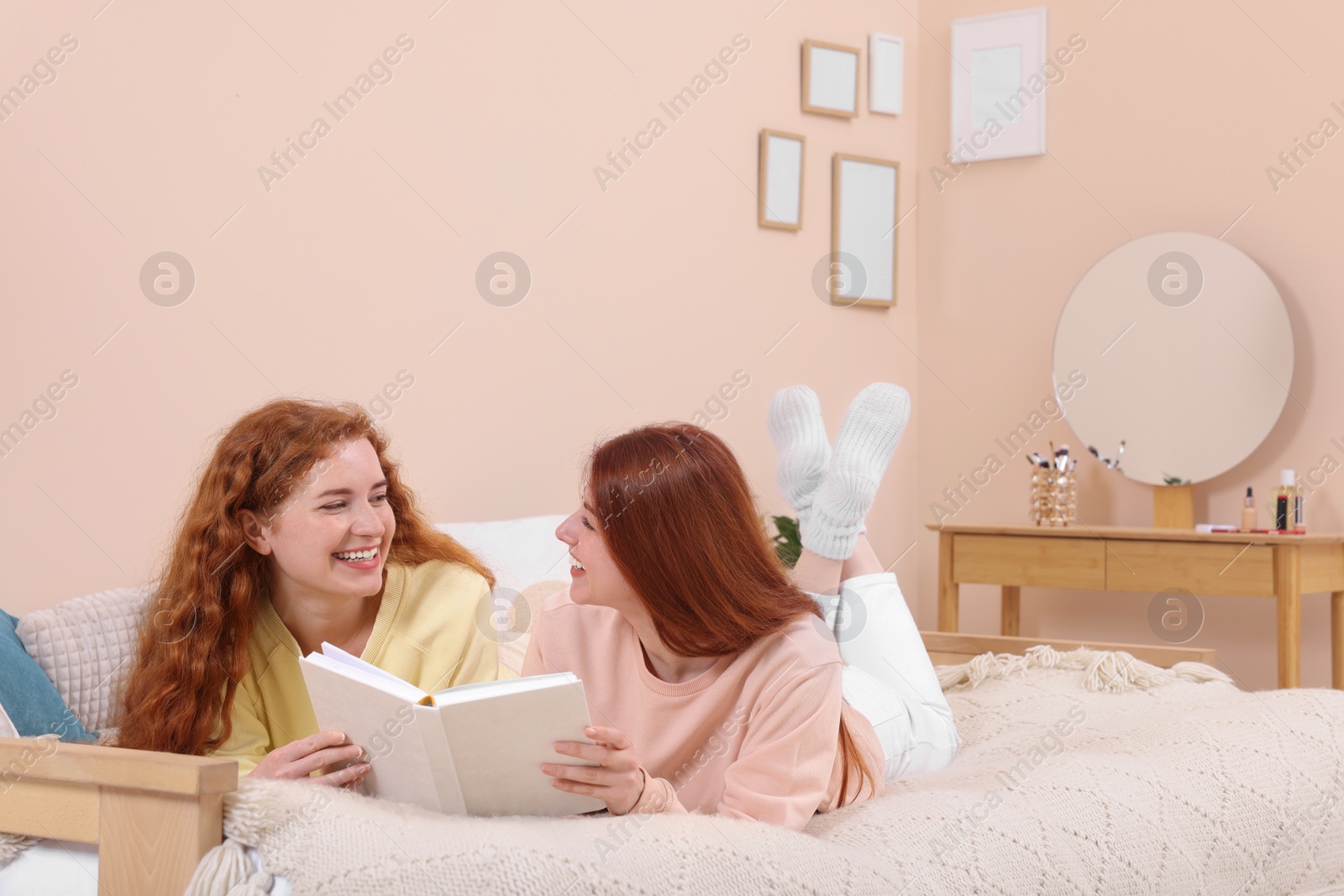 Photo of Beautiful young sisters reading book on bed at home. Space for text