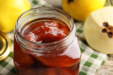 Photo of Tasty homemade quince jam in jar and fruits on table, closeup