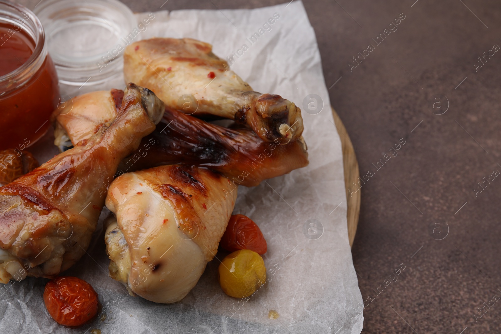 Photo of Marinade, roasted chicken drumsticks and tomatoes on brown table. Space for text
