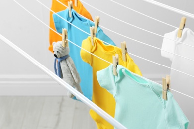 Different cute baby onesies and toy bear hanging on clothes line. Laundry day