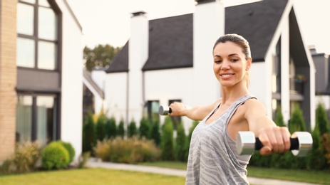 Photo of Sporty woman doing exercise with dumbbells on backyard. Healthy lifestyle