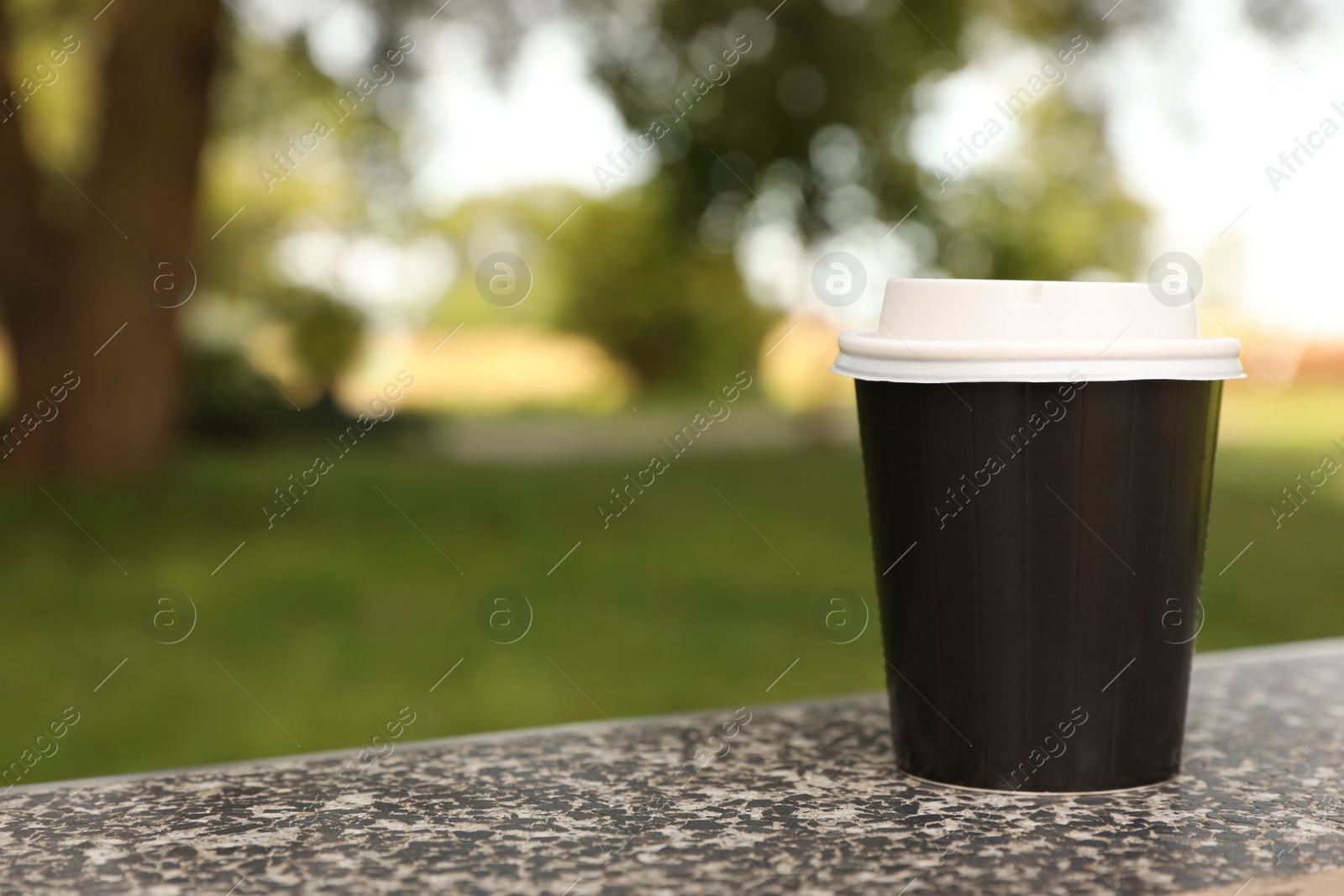 Photo of Paper cup on parapet in park, space for text. Coffee to go