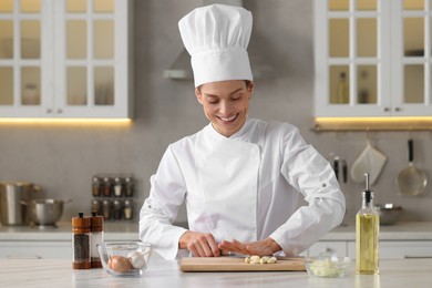 Professional chef cutting garlic at white marble table indoors