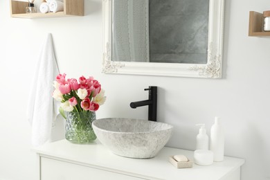 Photo of Vase with beautiful pink tulips and toiletries near sink in bathroom