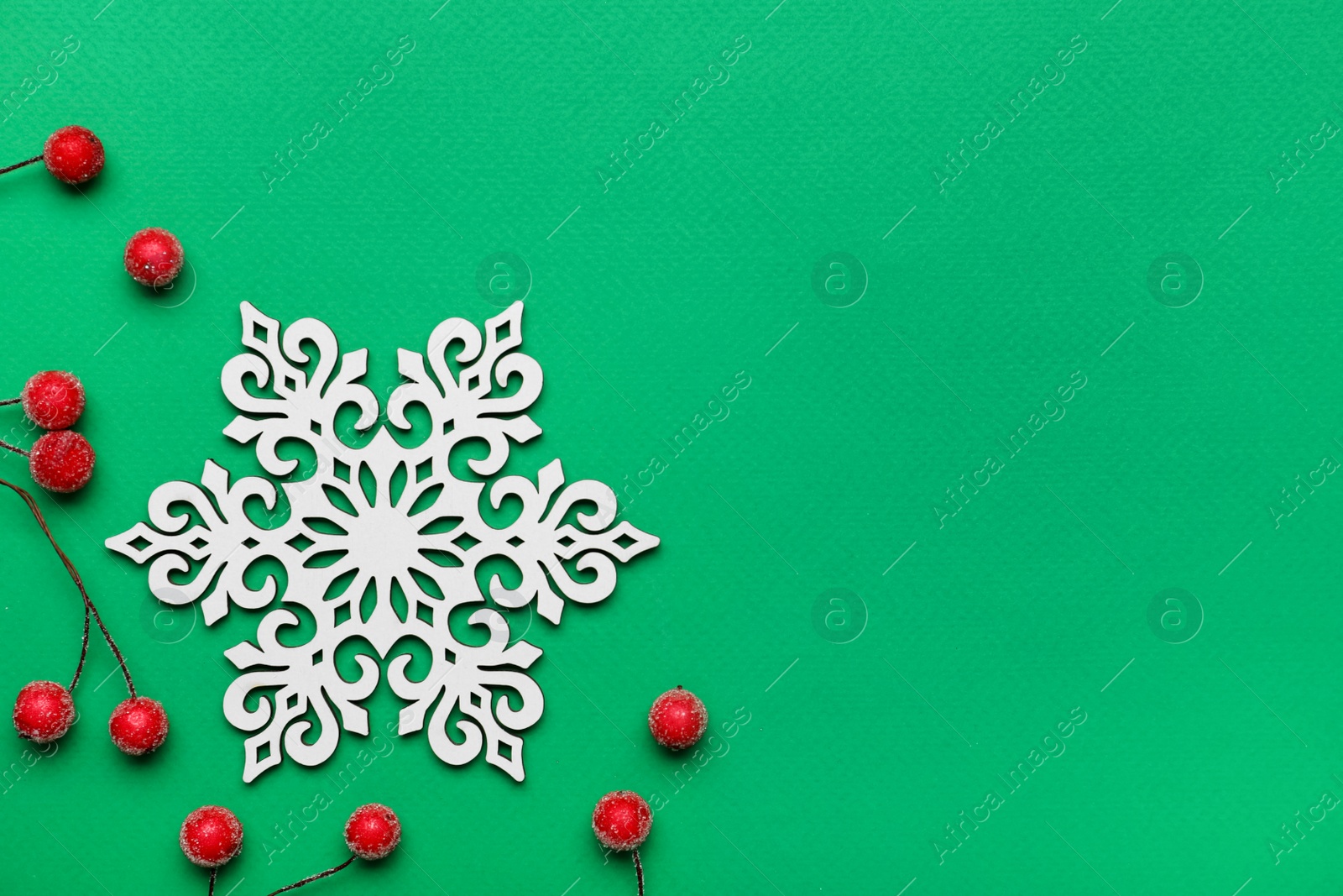 Photo of Beautiful decorative snowflake and red berries on green background, flat lay. Space for text