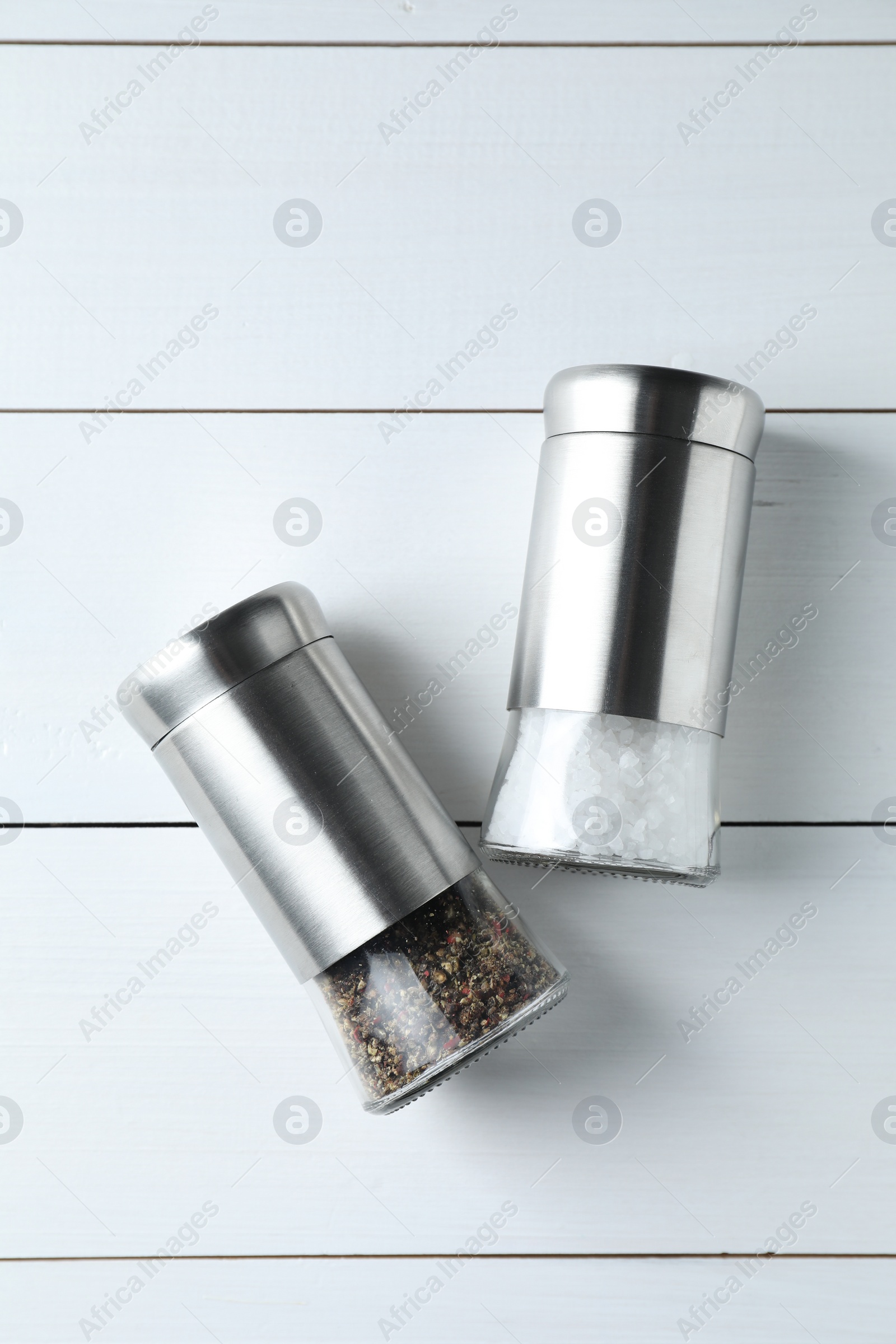 Photo of Salt and pepper shakers on white wooden table, flat lay