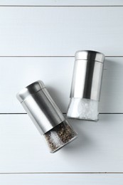 Photo of Salt and pepper shakers on white wooden table, flat lay